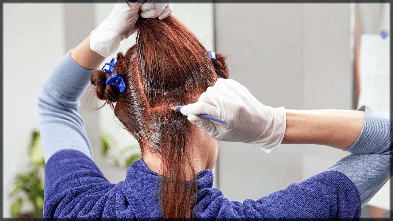 تصویری از یک خانم که درحال رنگ کردن ریشه ی موهای خود همراه با قلم و دستکش است، موهای او به رنگ قهوه ای است، موهای او بلند است و به سه قسمت تقسیم کرده است.